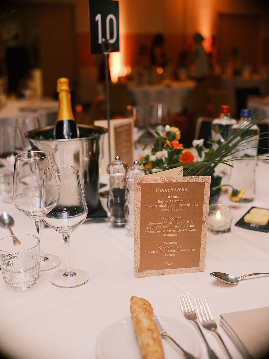 Table detail with the dinner menu card, champagne in an ice bucket and a low arrangement of flowers