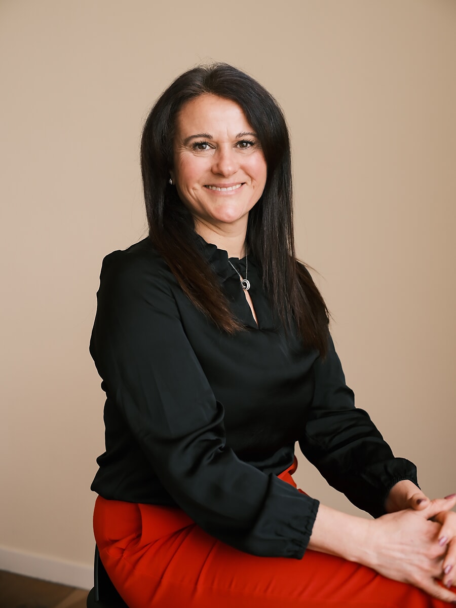 Colleague in a black blouse and red trousers seated with her hands clasped, a team photo for an Amsterdam business