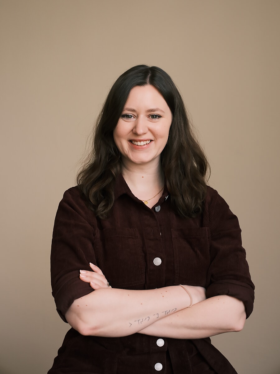 Colleague in a dark corduroy shirt with her arms folded, a small forearm tattoo showing
