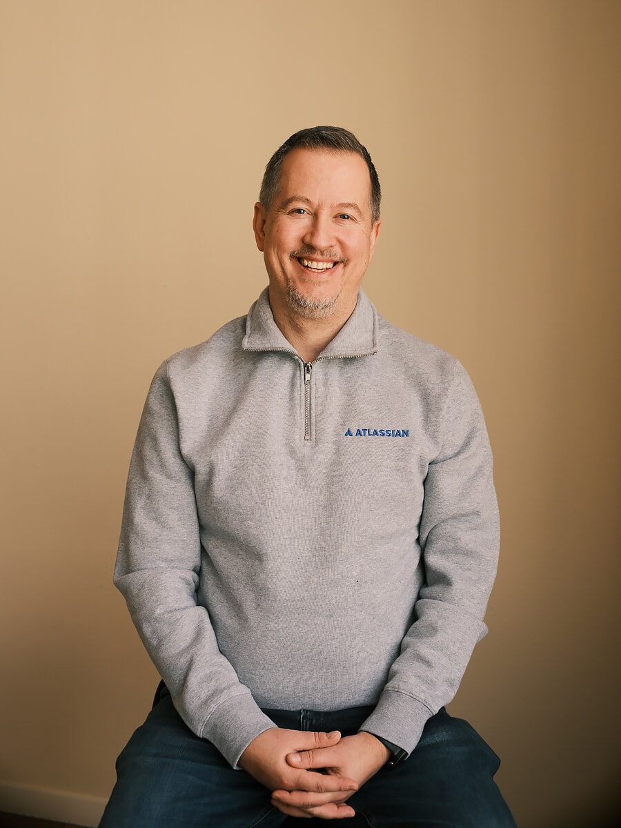 Colleague in a grey zip-neck sweater laughing mid-sentence, hands clasped, a team photoshoot for an Amsterdam business