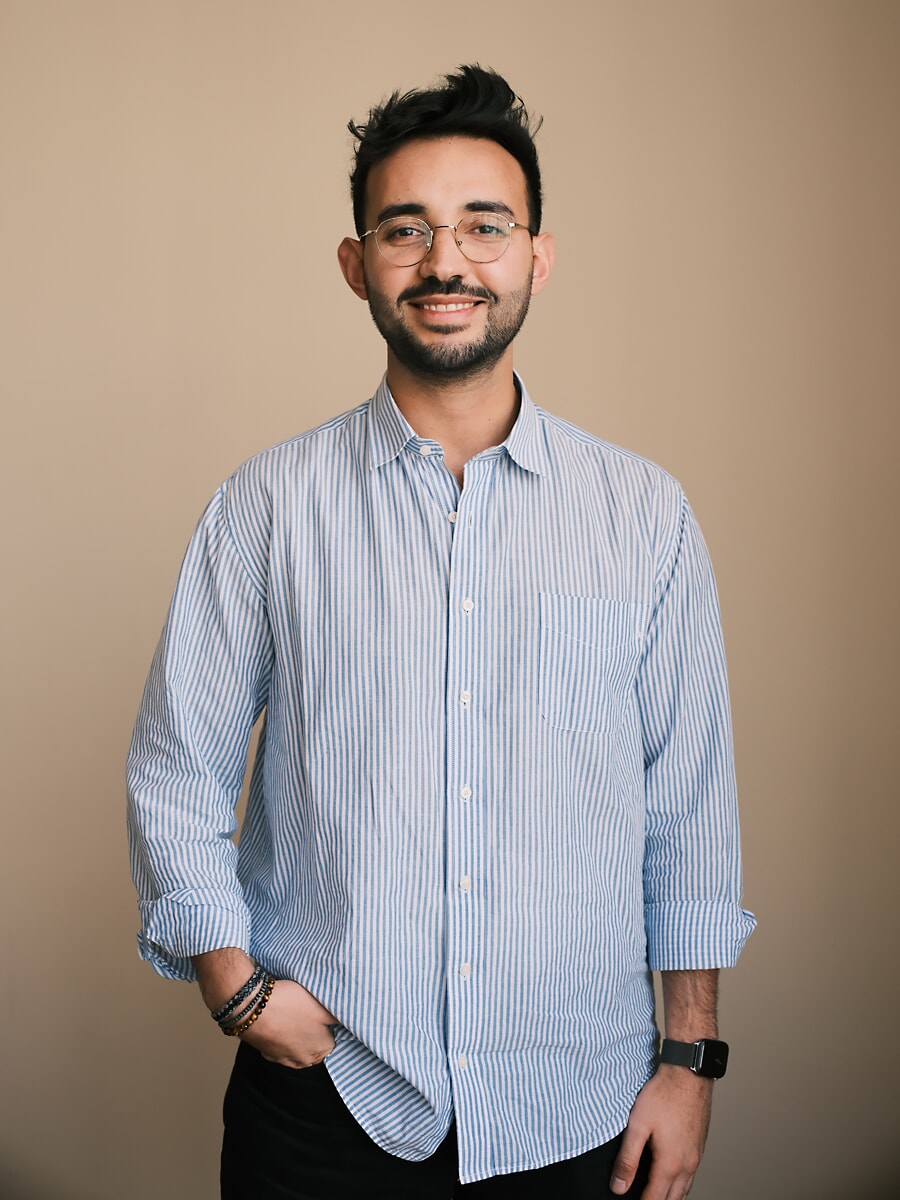 Colleague in a blue-striped shirt and round glasses standing with one hand in his pocket