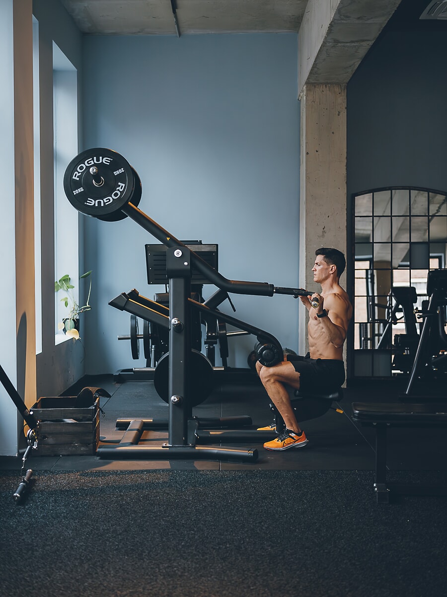 Trainer working on a plate-loaded machine in a concrete gym, weight plates against a pale blue wall, branding photography for an Amsterdam business
