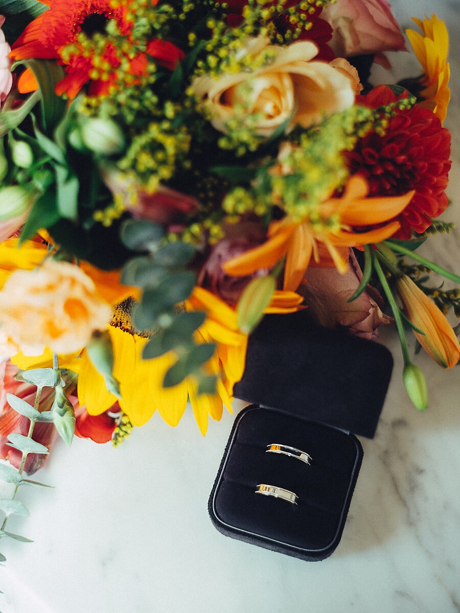 Wedding Ceremony SP15 Gold wedding bands in a black ring box beside an autumn bouquet of roses and sunflowers, a styled detail from the wedding photography