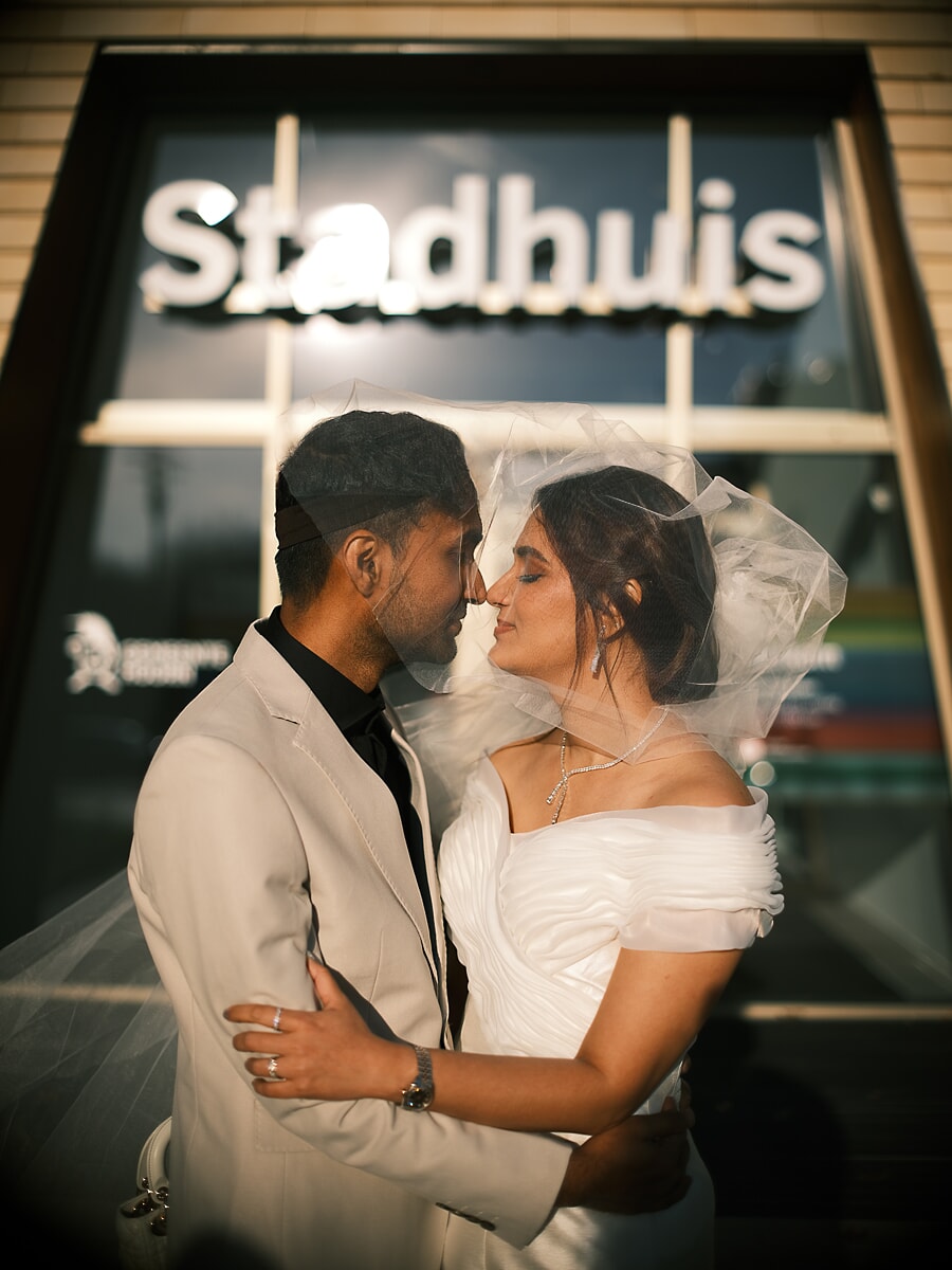 Wedding Ceremony SP2 Newlyweds touching foreheads beneath the veil outside an illuminated Stadhuis city hall at dusk, a tender moment from their wedding photoshoot