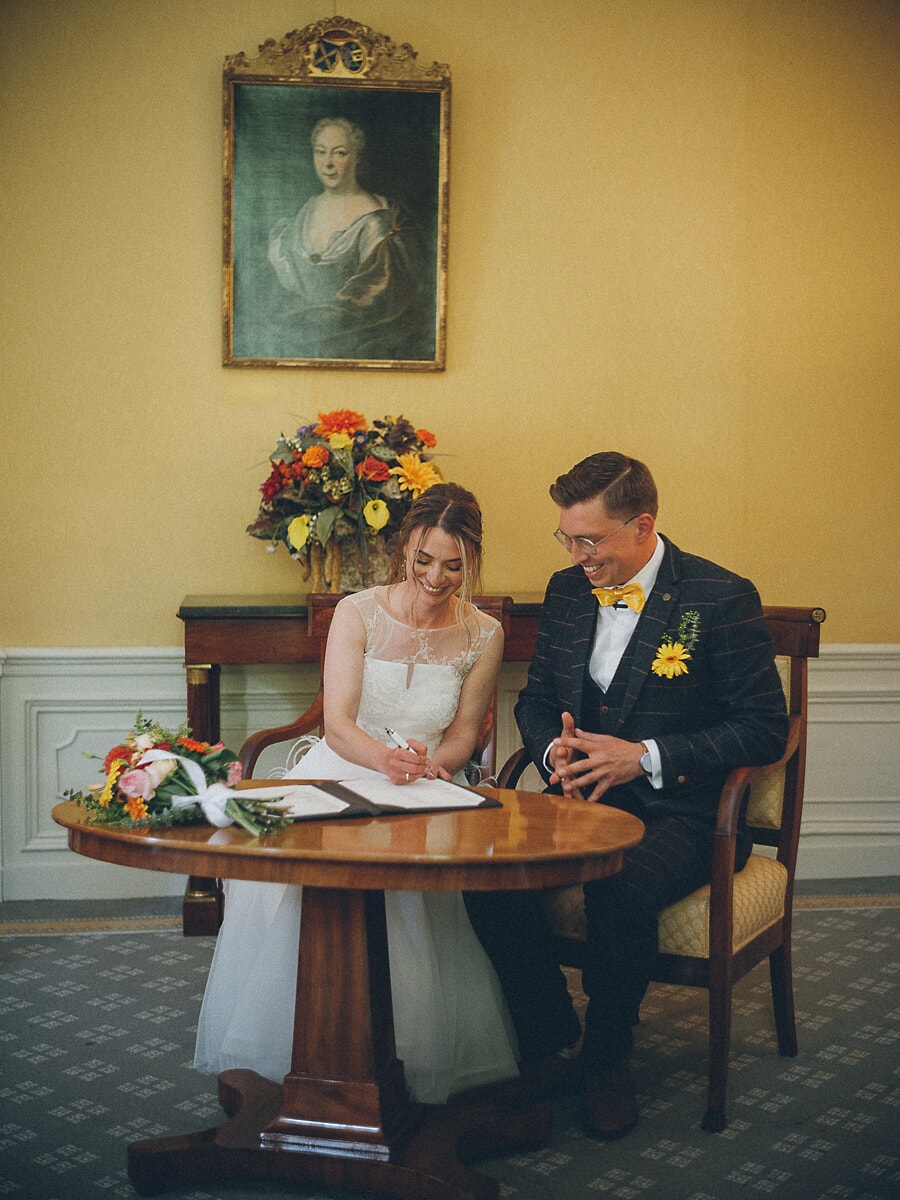 Wedding Ceremony SP22 Bride signs the marriage register beside her groom, an autumn bouquet at her side, captured by a wedding photographer in Amsterdam
