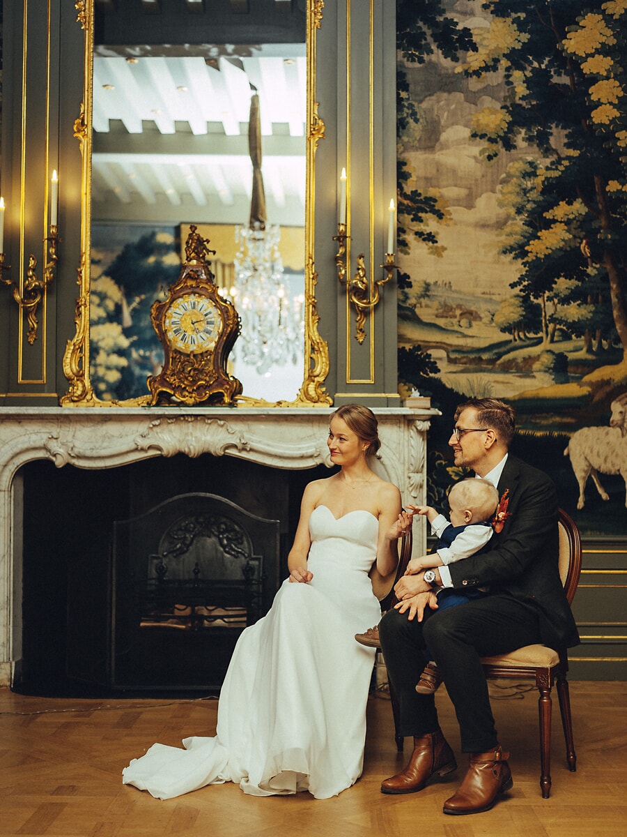 Wedding Ceremony SP24 Bride, groom and their baby seated before an ornate gilded mirror and mantel clock, an elegant civil wedding portrait