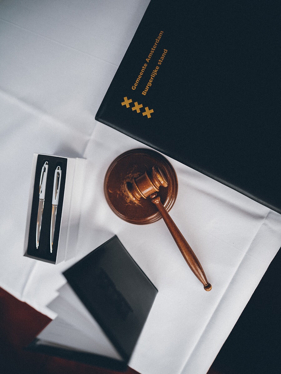 Wedding Ceremony SP31 Amsterdam municipal marriage register in a black Gemeente Amsterdam folder beside a wooden gavel and engraved pens, a civil wedding photo detail