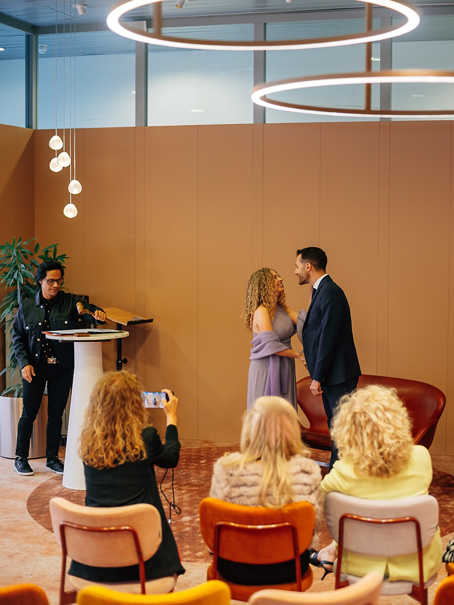 Wedding Ceremony SP32 Couple exchange vows in a modern venue lit by ring pendants, guests watching, a candid frame by a wedding photographer in Amsterdam