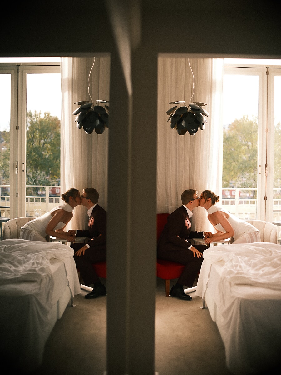 Wedding Bridal SP1 Couple kiss on a red sofa in a sunlit room, their moment doubled in a mirror, by a wedding photographer in Amsterdam