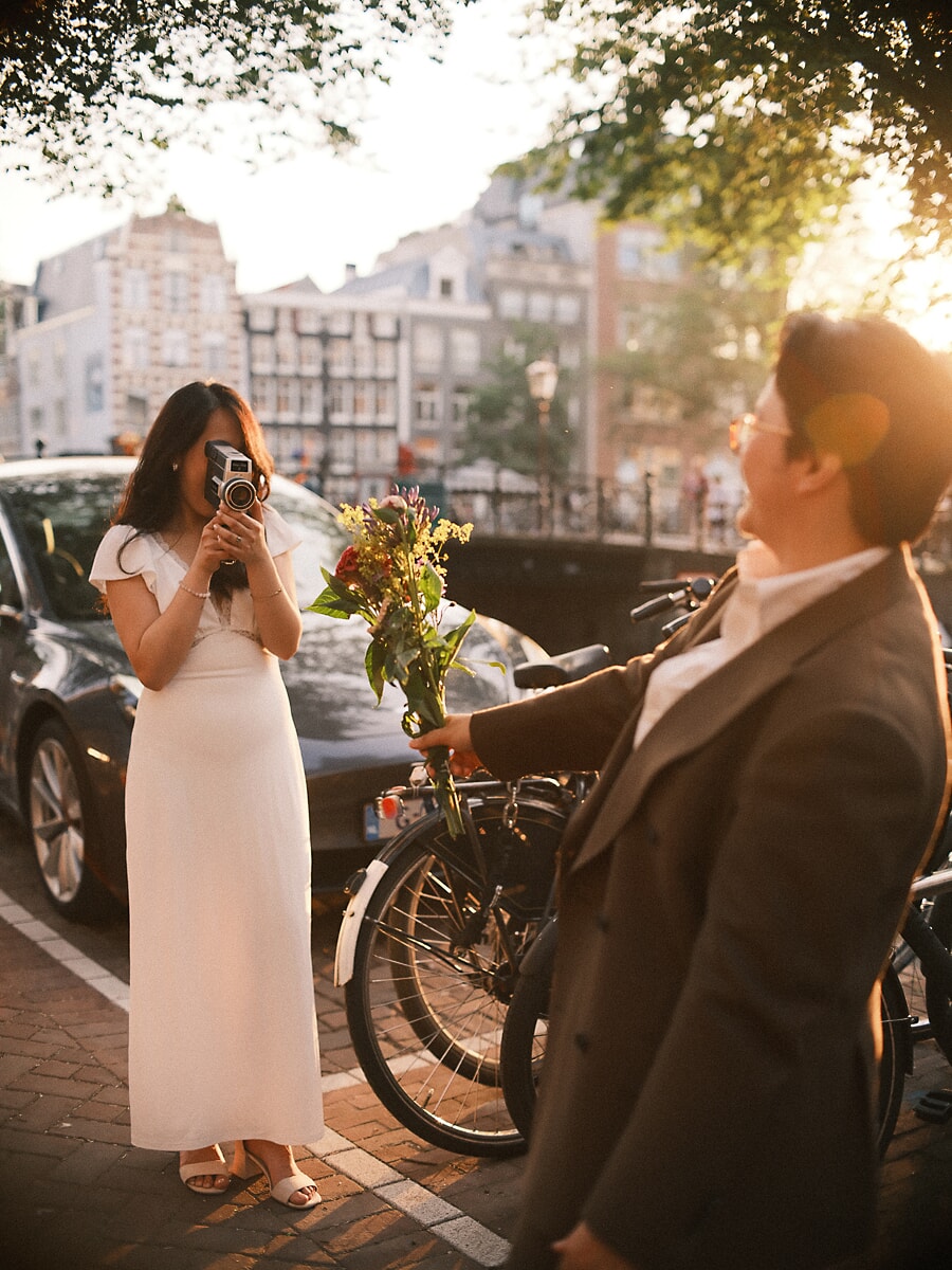 Wedding Bridal SP11 Bride films her laughing groom on a vintage cine camera along a canal street, an elopement shoot with a wedding photographer in Amsterdam