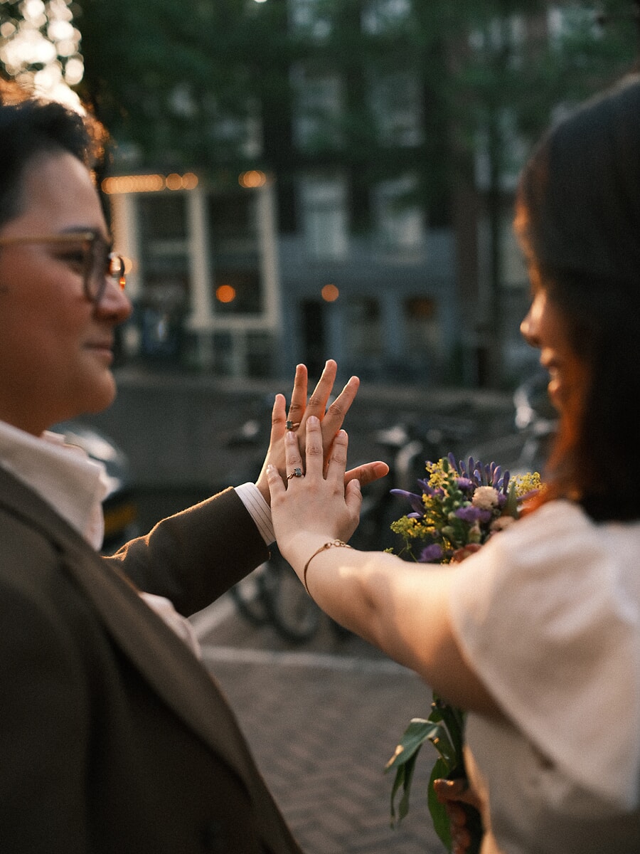 Wedding Bridal SP13 Palms pressed together to show their rings on a canal street, the newlyweds hold a wildflower bouquet, a tender elopement detail