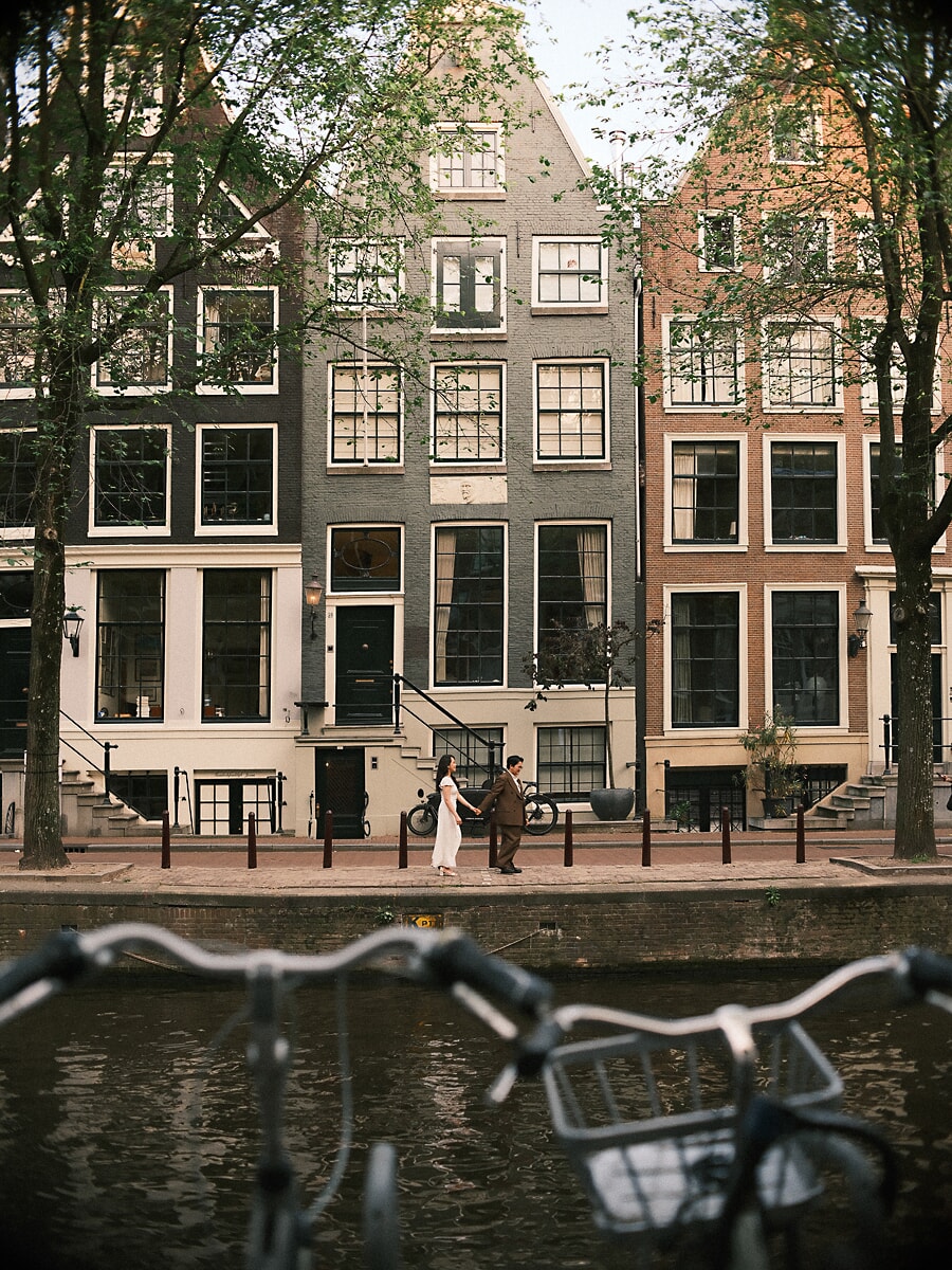 Wedding Bridal SP16 Seen past blurred bicycle handlebars, the newlyweds stroll the quay beneath tall canal houses, a documentary style elopement photograph