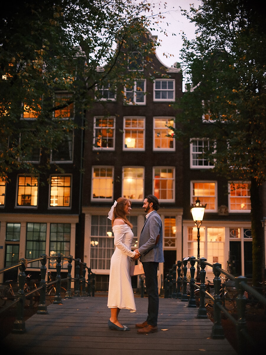 Wedding Bridal SP7 Facing each other on a canal bridge at dusk with warm light glowing from the windows behind, a tender frame from the bridal session