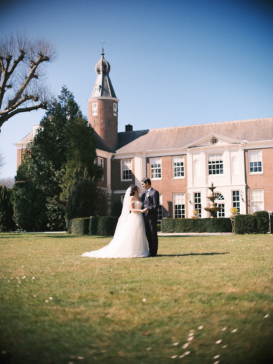 Wedding Bridal SP22 Holding hands on the lawn of a Dutch country manor under a blue sky, the couple pose for a wedding photographer in Amsterdam