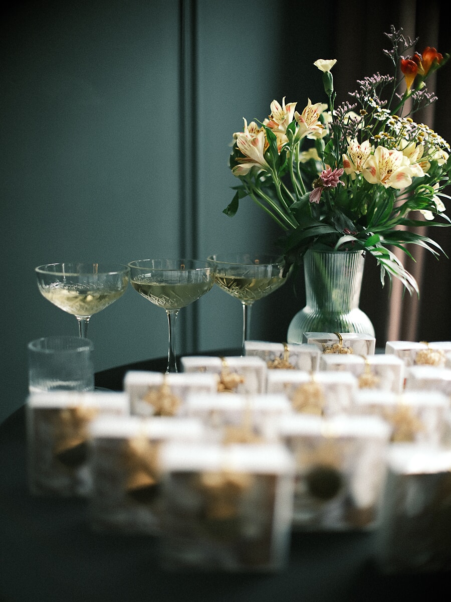 Wedding SP12 Champagne coupes and glass jar favours arranged around a fluted vase of flowers on a dark reception table, a styled wedding detail