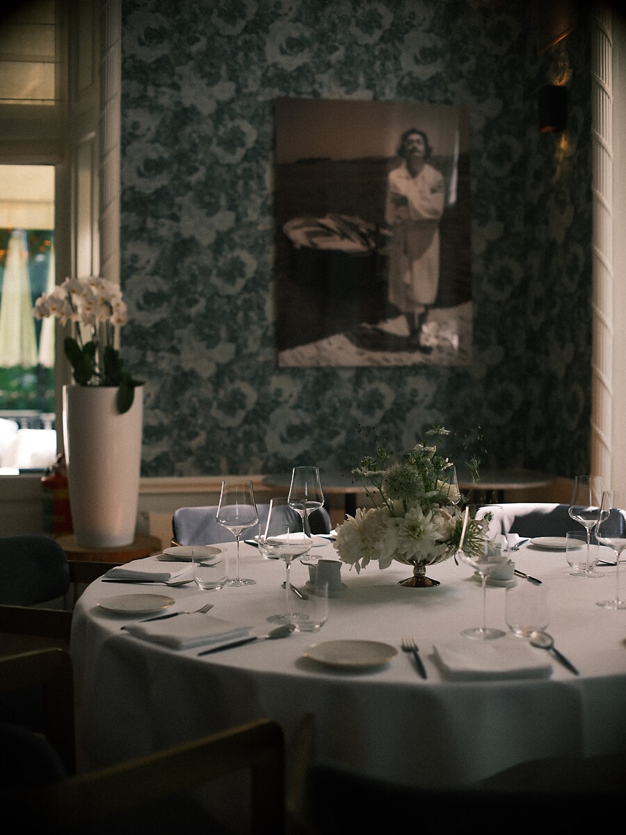 Wedding SP14 Round table dressed with white blooms and crystal glasses before floral wallpaper, a refined reception photo