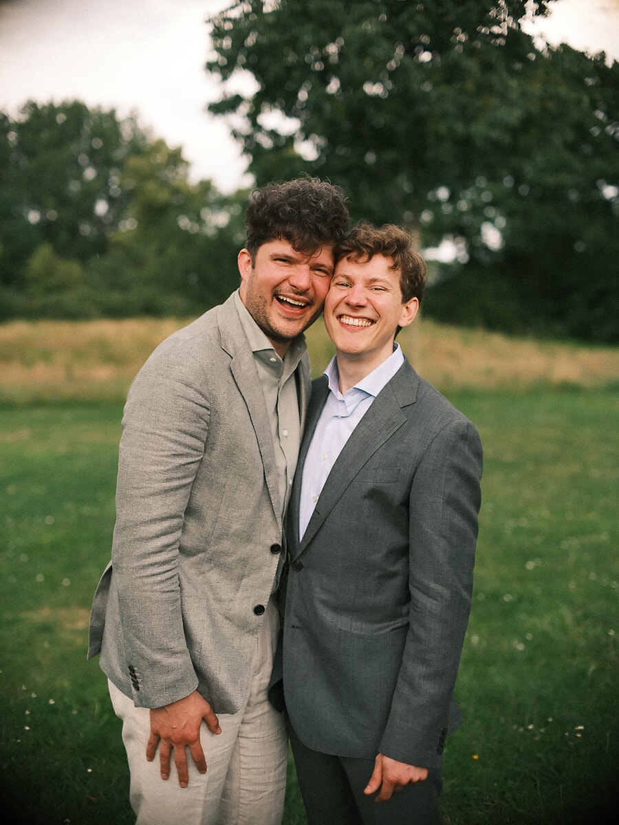 Wedding SP15 Two grooms in grey and linen suits laugh cheek to cheek, an LGBTQ+ couple photographed by a wedding photographer in Amsterdam
