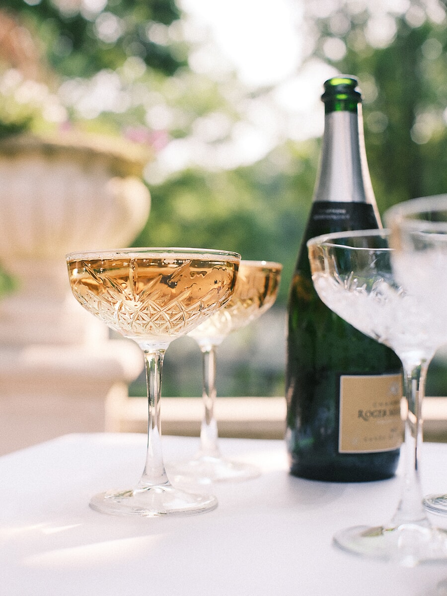 Wedding SP17 Chilled champagne bottle beside two filled crystal coupes on a sunlit terrace table, a celebratory detail from the wedding photo session