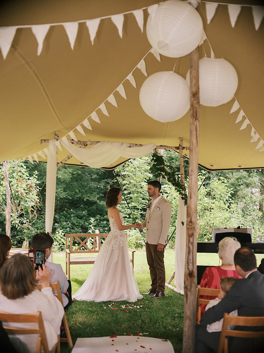 Wedding SP19 A wedding photographer in Amsterdam documents the couple holding hands under paper lanterns and bunting in a garden marquee