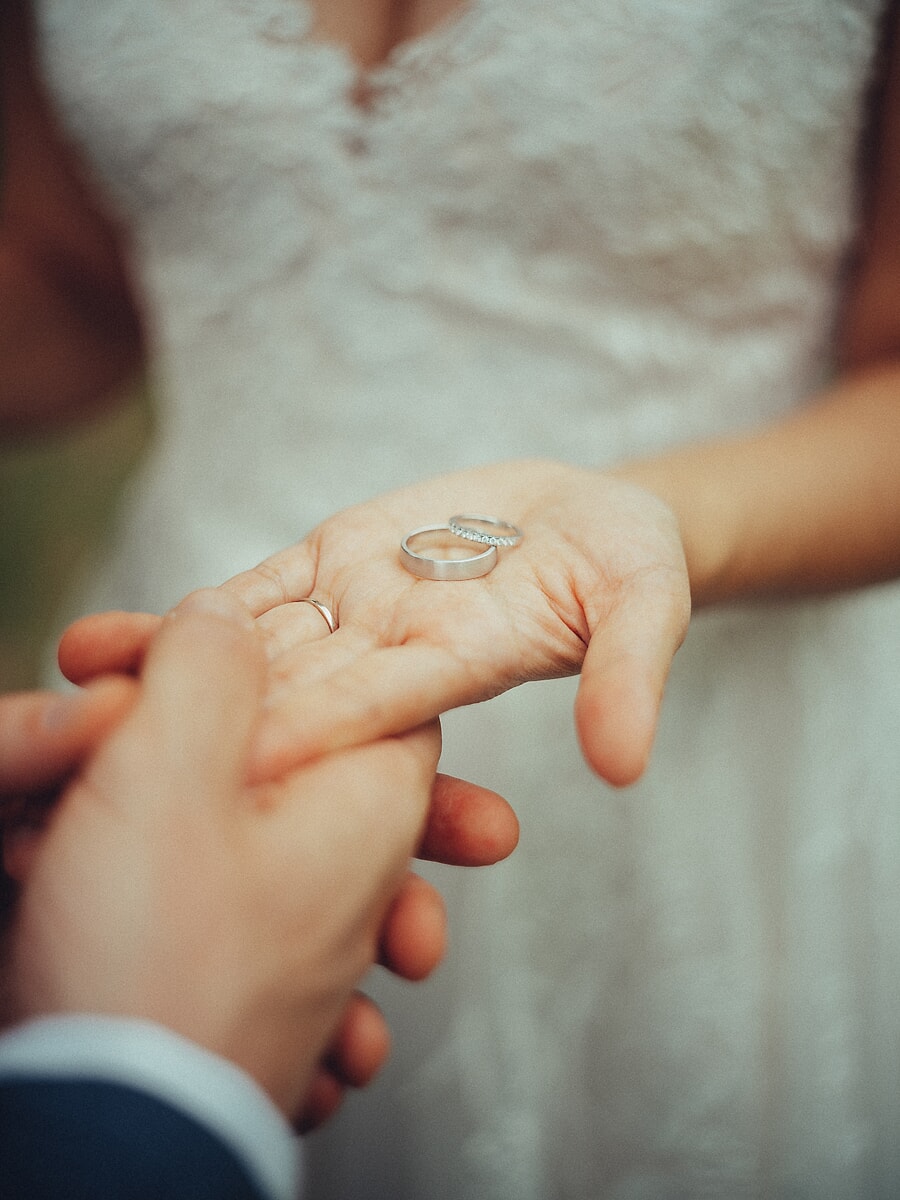 Wedding SP28 Close-up of the bride holding a wedding band in her open palm above her groom's hand, an intimate ring detail