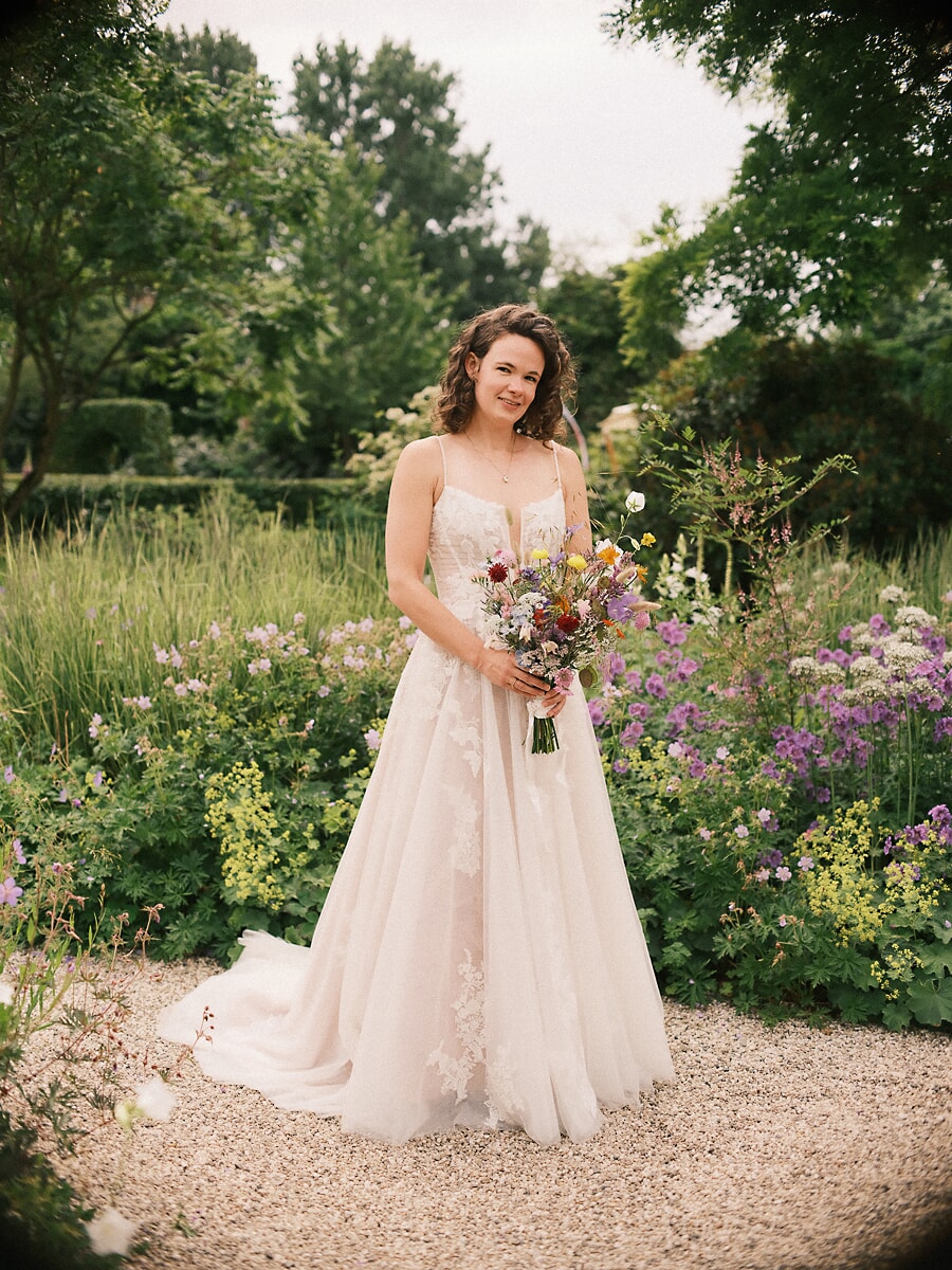 Wedding SP3 Holding a wildflower bouquet on a gravel path in a summer garden, the bride smiles for a wedding photographer in Amsterdam