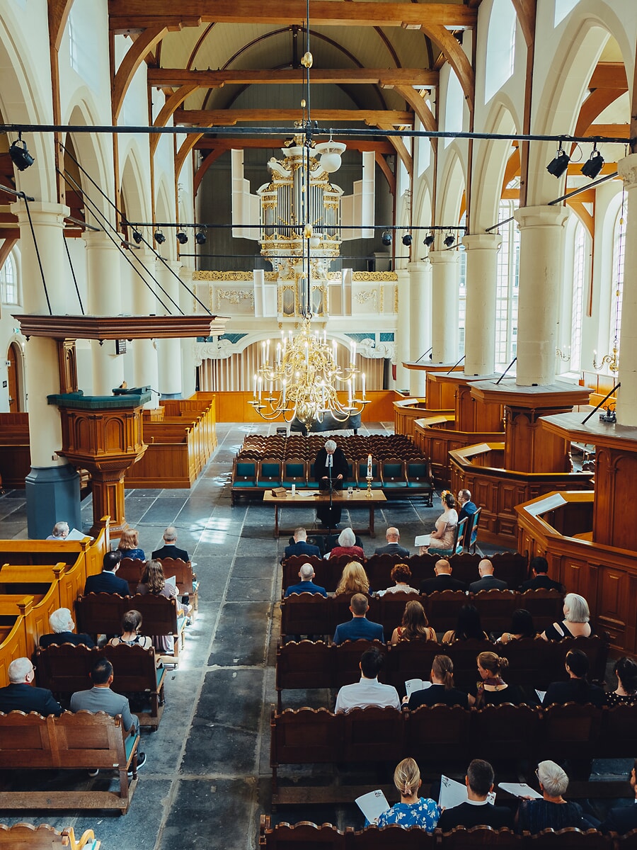 Wedding SP32 Historic Dutch church with wooden pews and a gilded chandelier fills with guests, a grand frame by a wedding photographer in Amsterdam