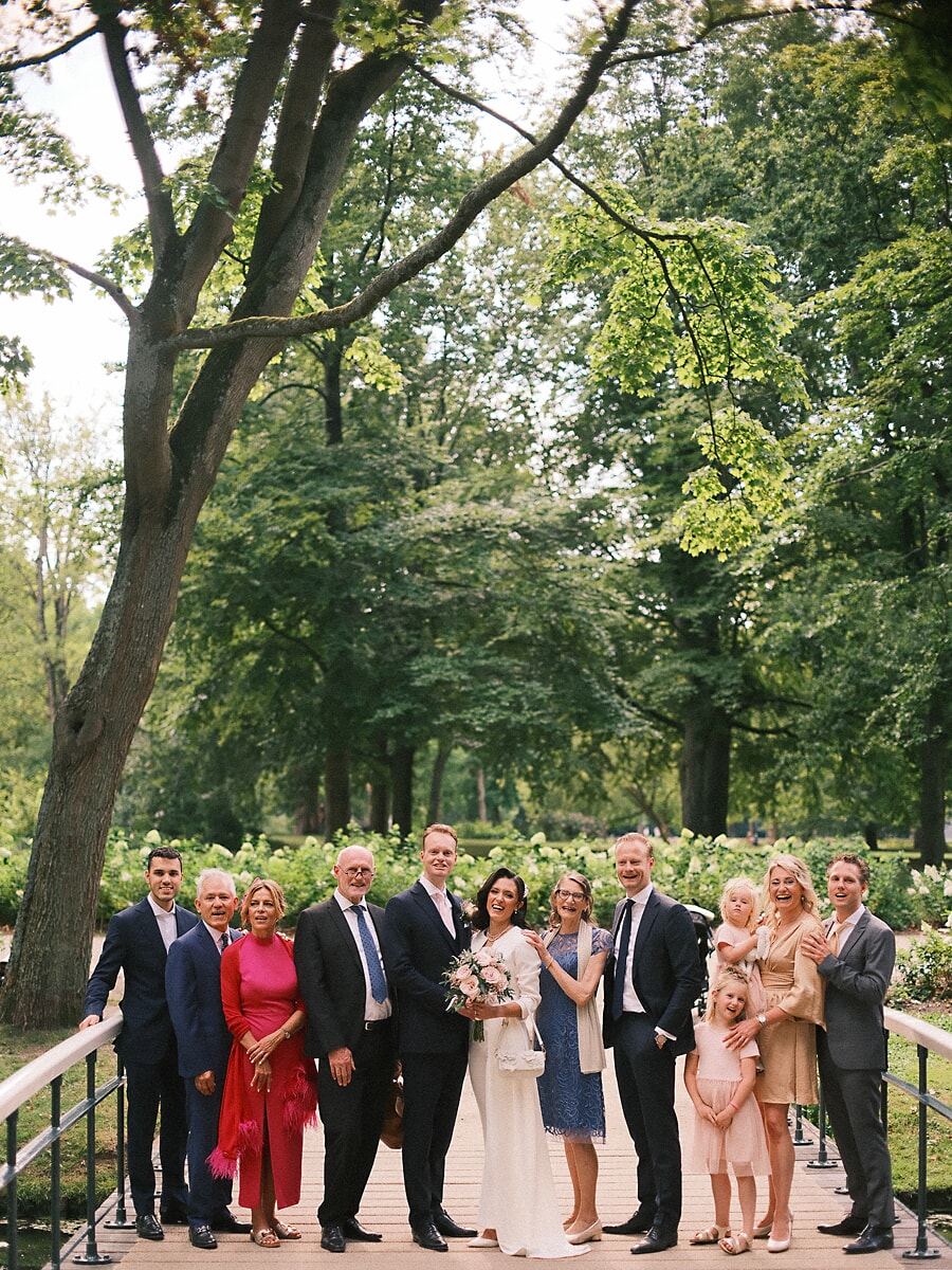 Wedding SP4 Family and friends gather around the couple on a wooden park bridge, a joyful group portrait from the wedding reportage
