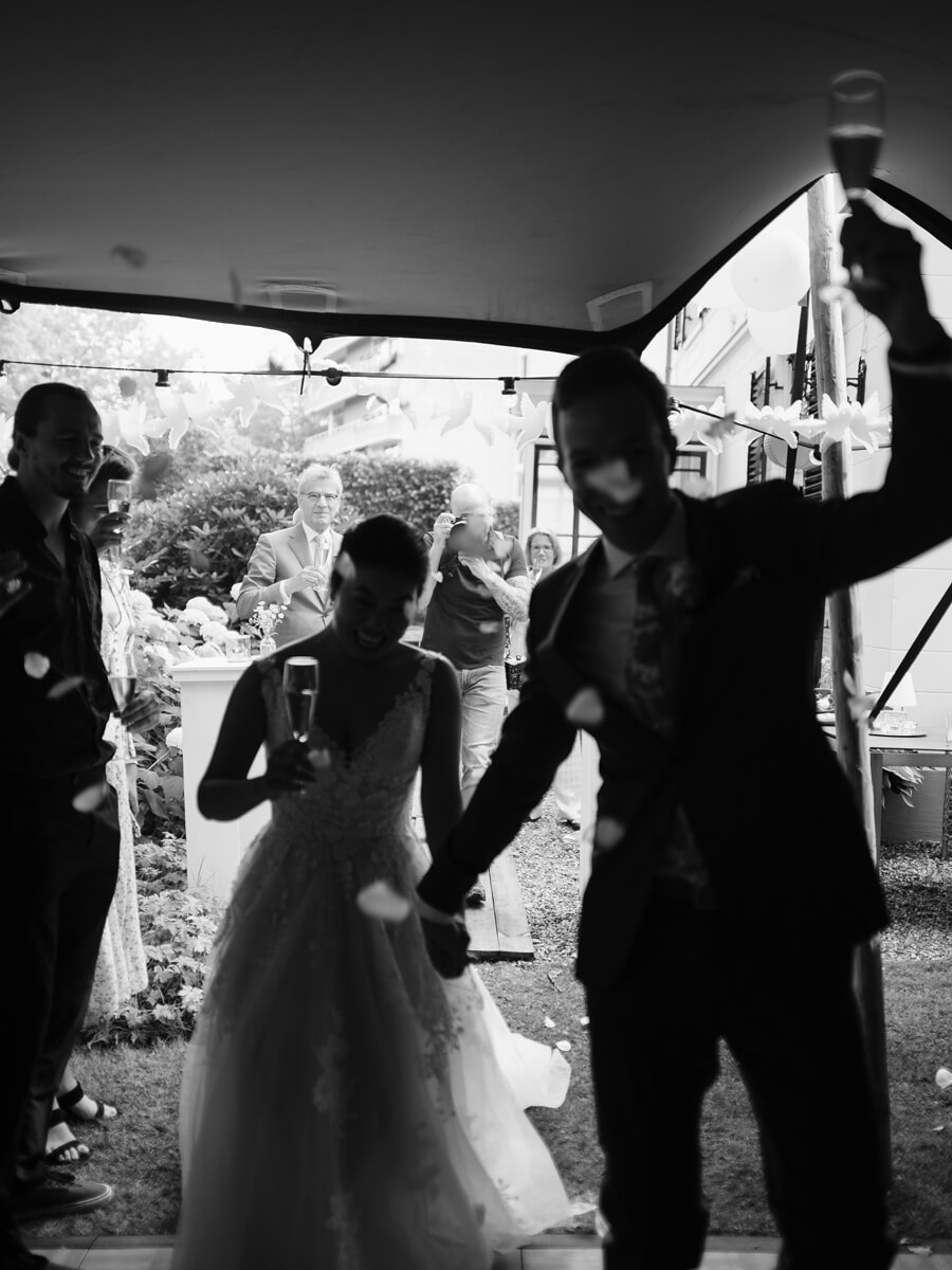 Wedding SP40 Black and white photo of the newlyweds stepping out with champagne as guests cheer, by a wedding photographer in Amsterdam