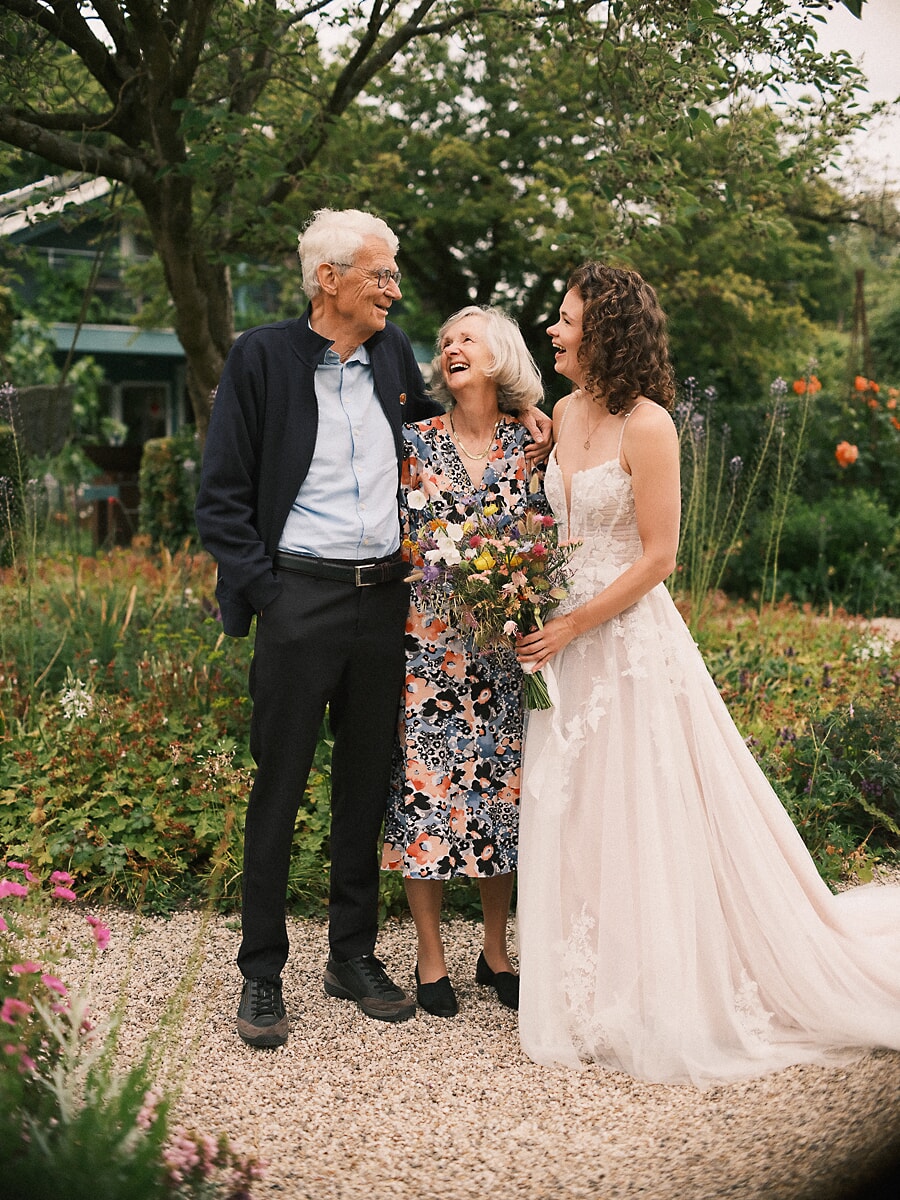 Wedding SP7 Arm in arm with her parents, the laughing bride holds wildflowers, a heartfelt frame by a wedding photographer in Amsterdam