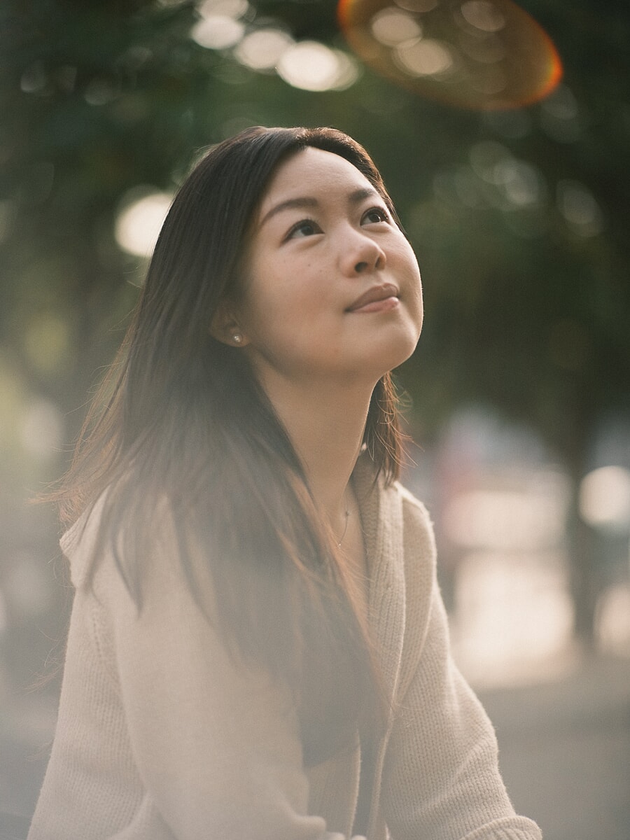 Woman in a cream cardigan looking up past the camera, an orange lens halo drifting across the corner of the frame