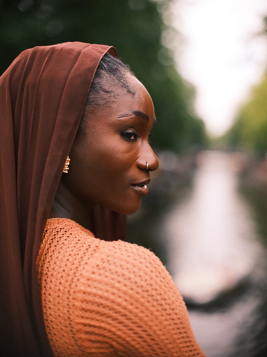 Profile of a woman in a rust head scarf looking down an Amsterdam canal, a quiet moment from her creative portrait session