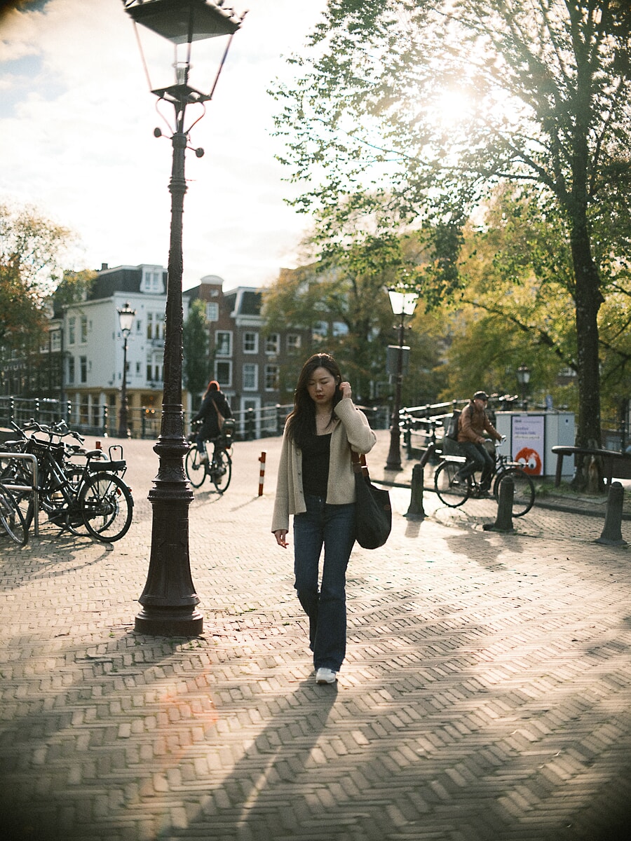 Woman in a cream cardigan walking across a brick square in low autumn sun, a relaxed dating portrait in Amsterdam