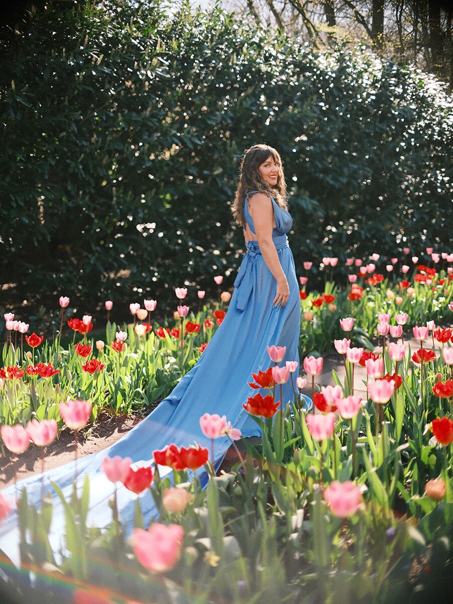 Woman looking back over her shoulder as the long train of her blue gown trails across a tulip bed at Keukenhof