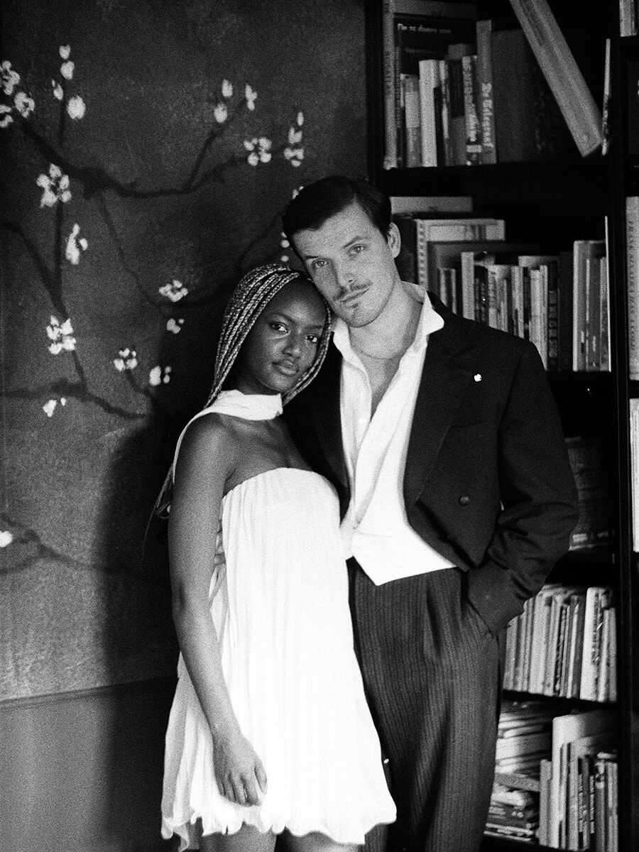 A couple rest their heads together beside a bookcase and floral wallpaper during an analog portrait session in Amsterdam