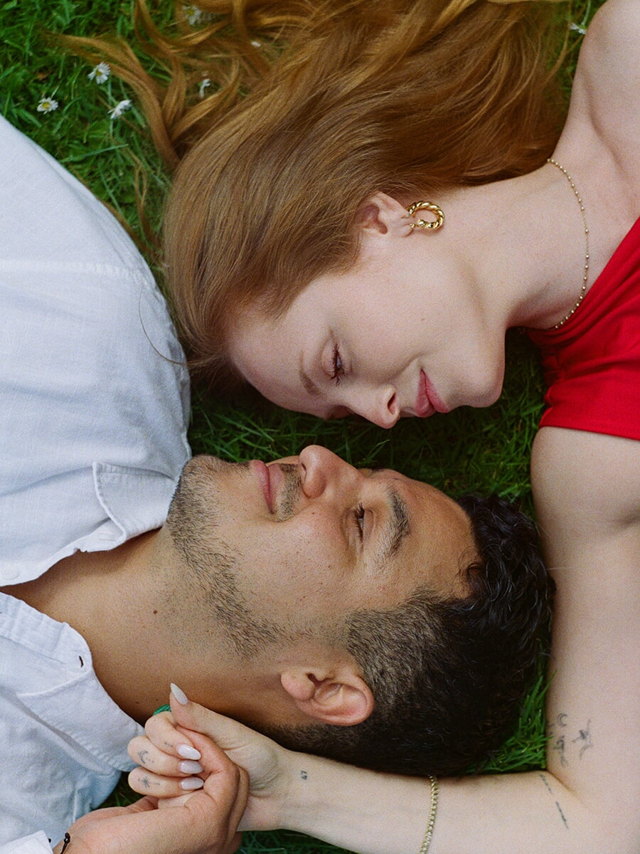 Overhead analog portrait of a couple lying hand in hand in the grass in Amsterdam, her red dress beside his white shirt