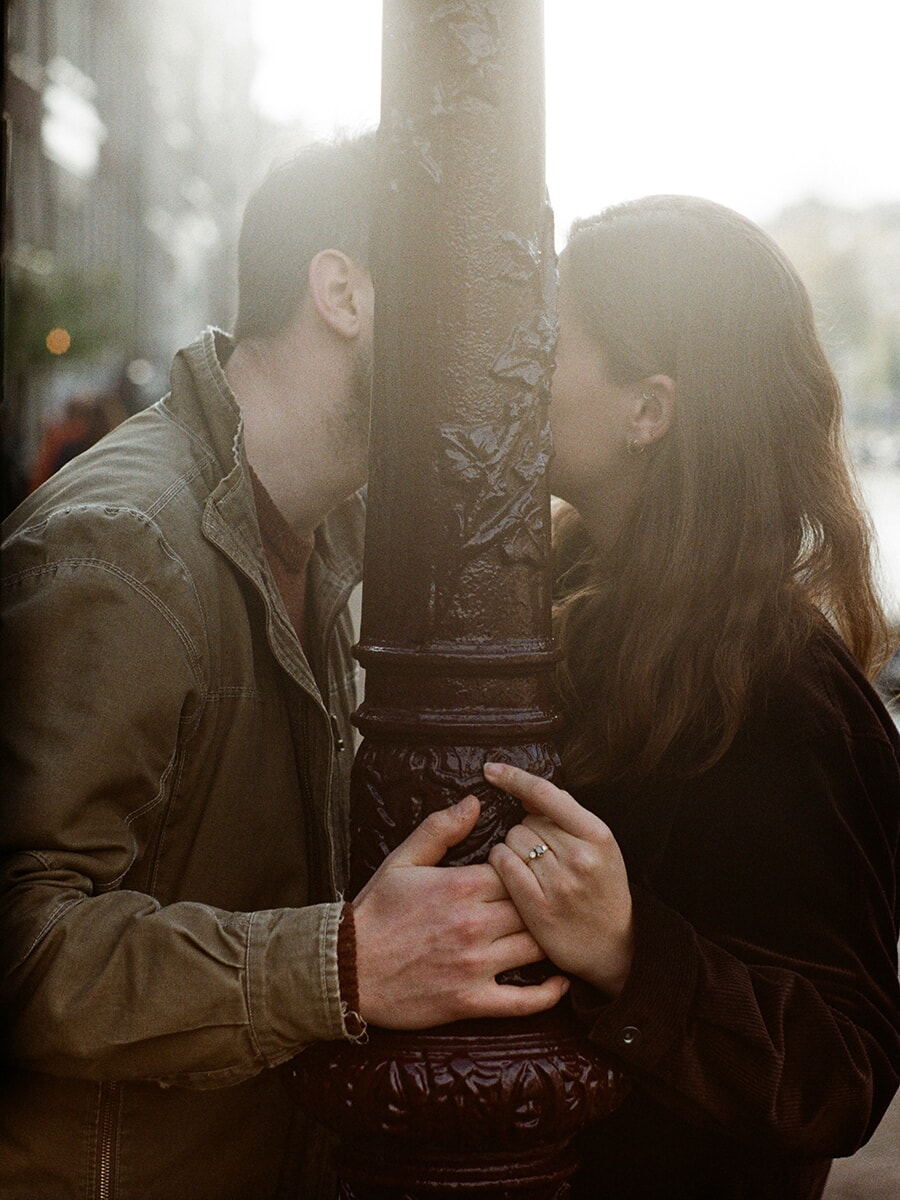 With their faces partly hidden by an ornate lamppost, a couple lean towards each other and join hands around it