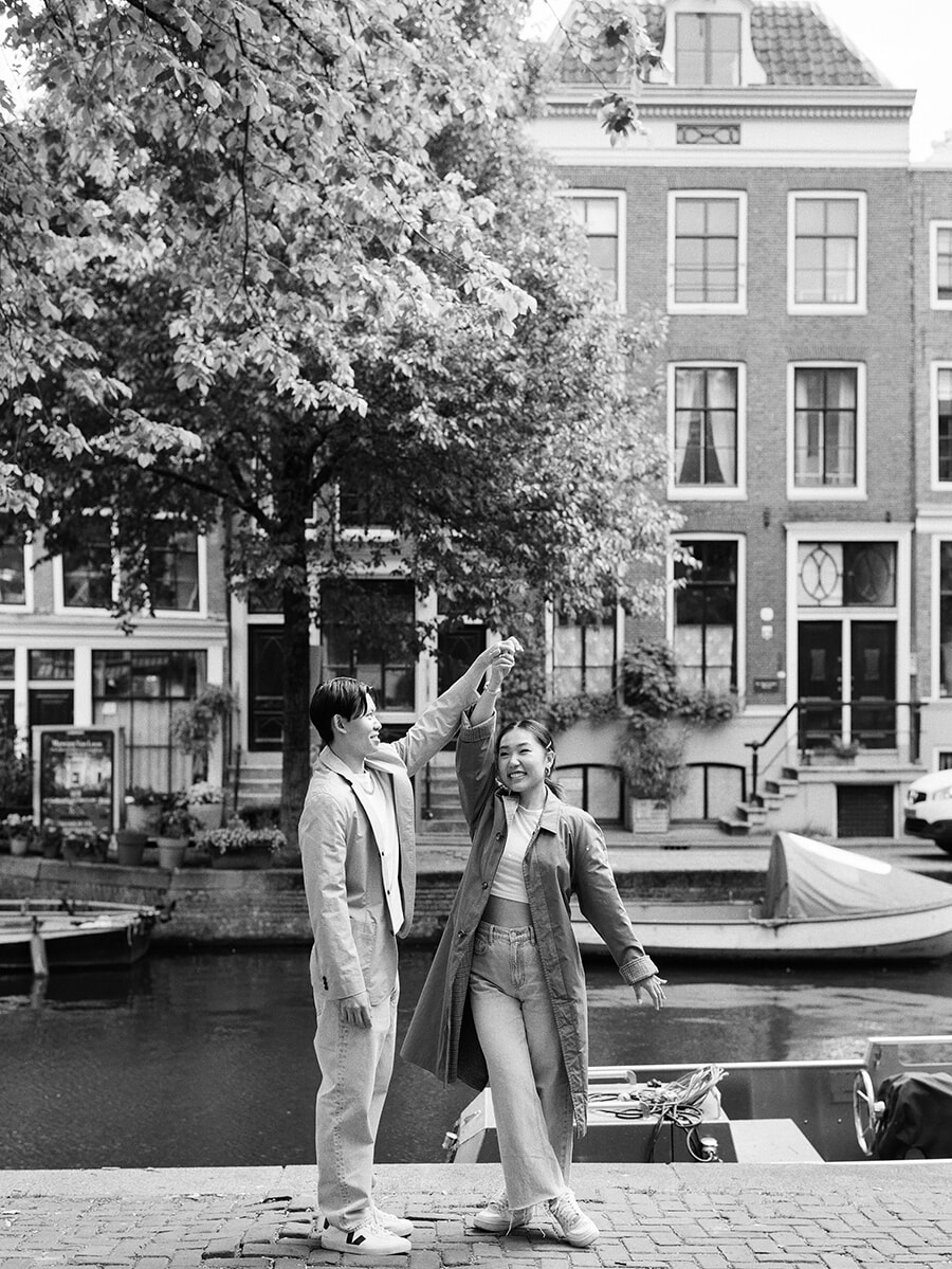 A woman twirls beneath her partner’s raised hand by an Amsterdam canal during an analog photoshoot