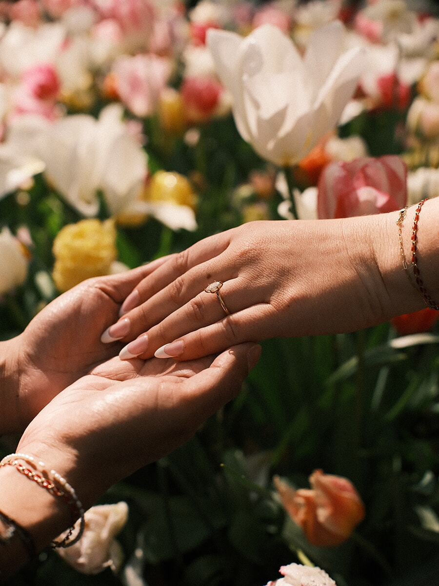 Her hand with a delicate gold engagement ring laid across his open palms, white and pink tulips softly blurred