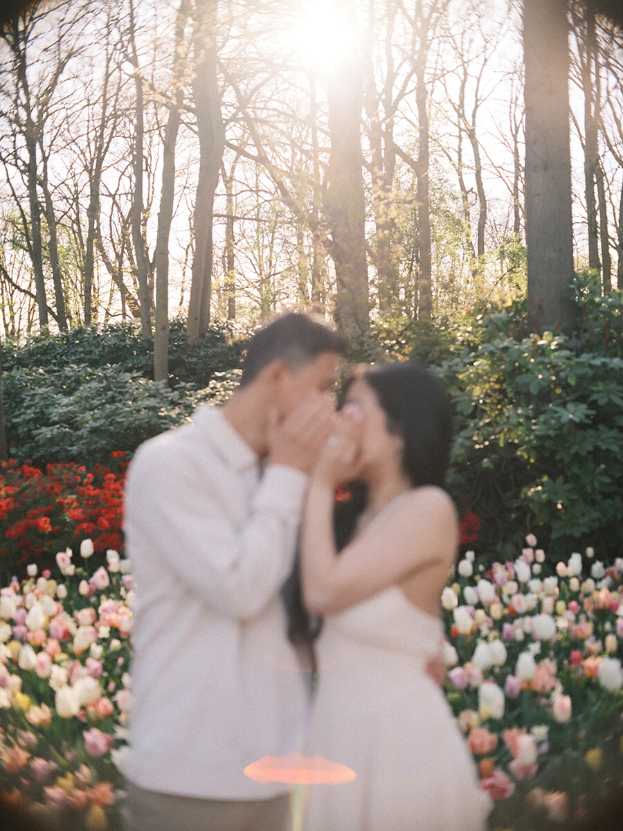 Dreamy out-of-focus moment as a couple lean in to kiss, the sun bursting through bare trees with an orange lens flare