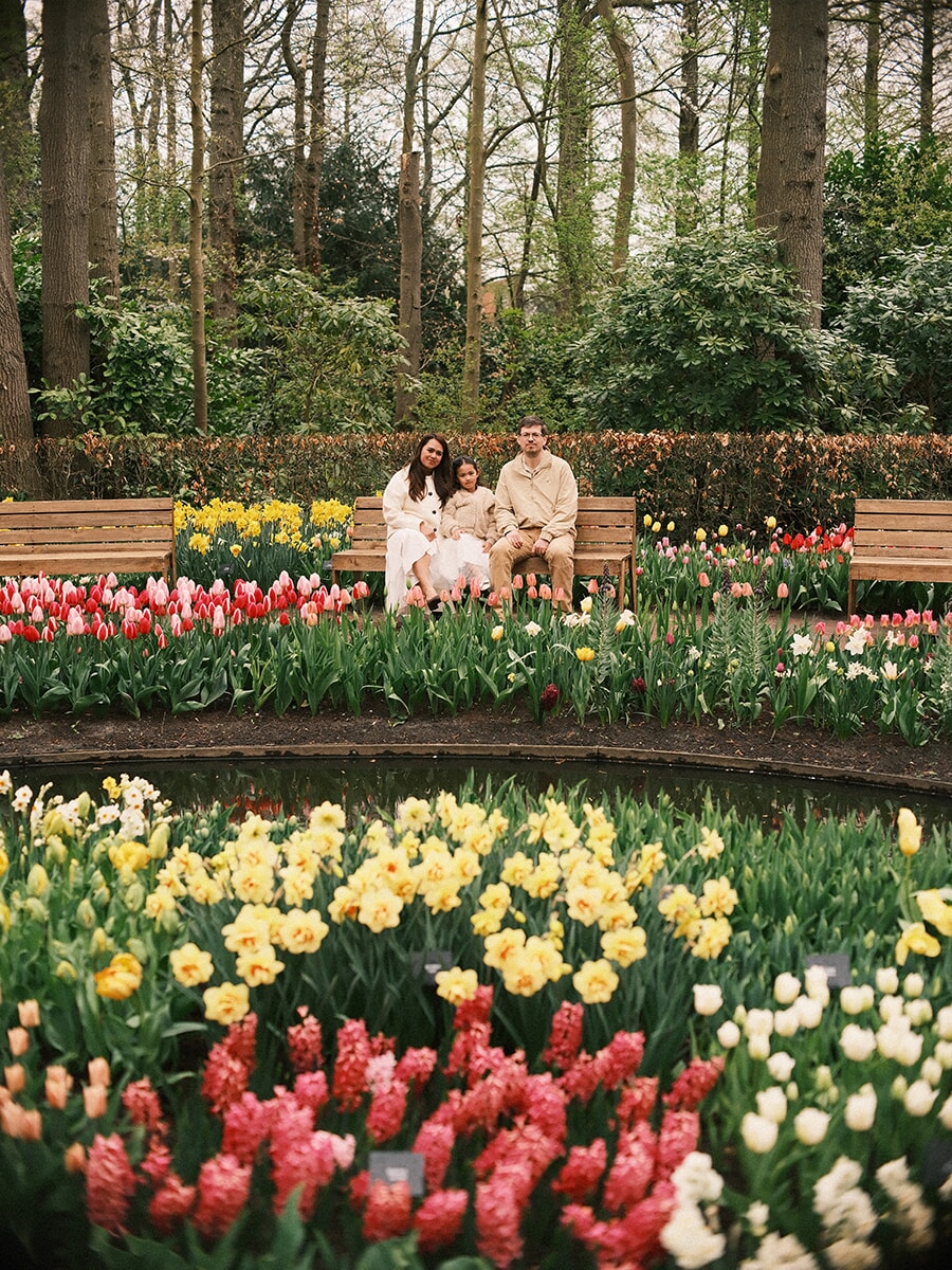 Parents and their little girl on a bench behind a round pond, layered narcissus, tulips and hyacinths in front at Keukenhof