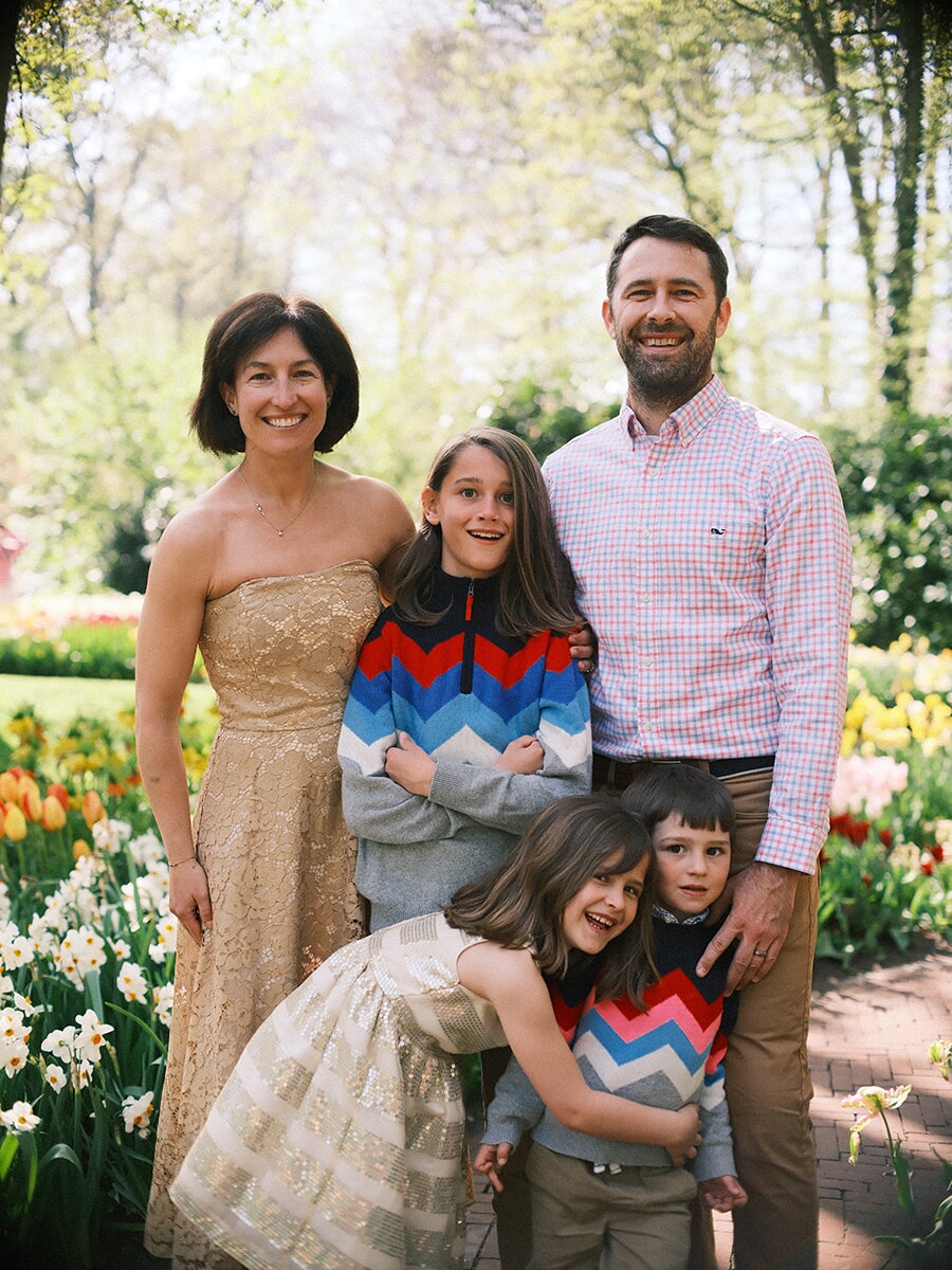 Family of five on a brick garden path, the children in zigzag sweaters and a gold dress, tulips and narcissus beside them