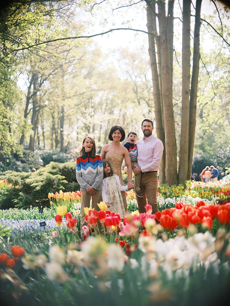 Family of five standing together in a tulip garden, father holding the youngest, red and orange tulips blurred in front