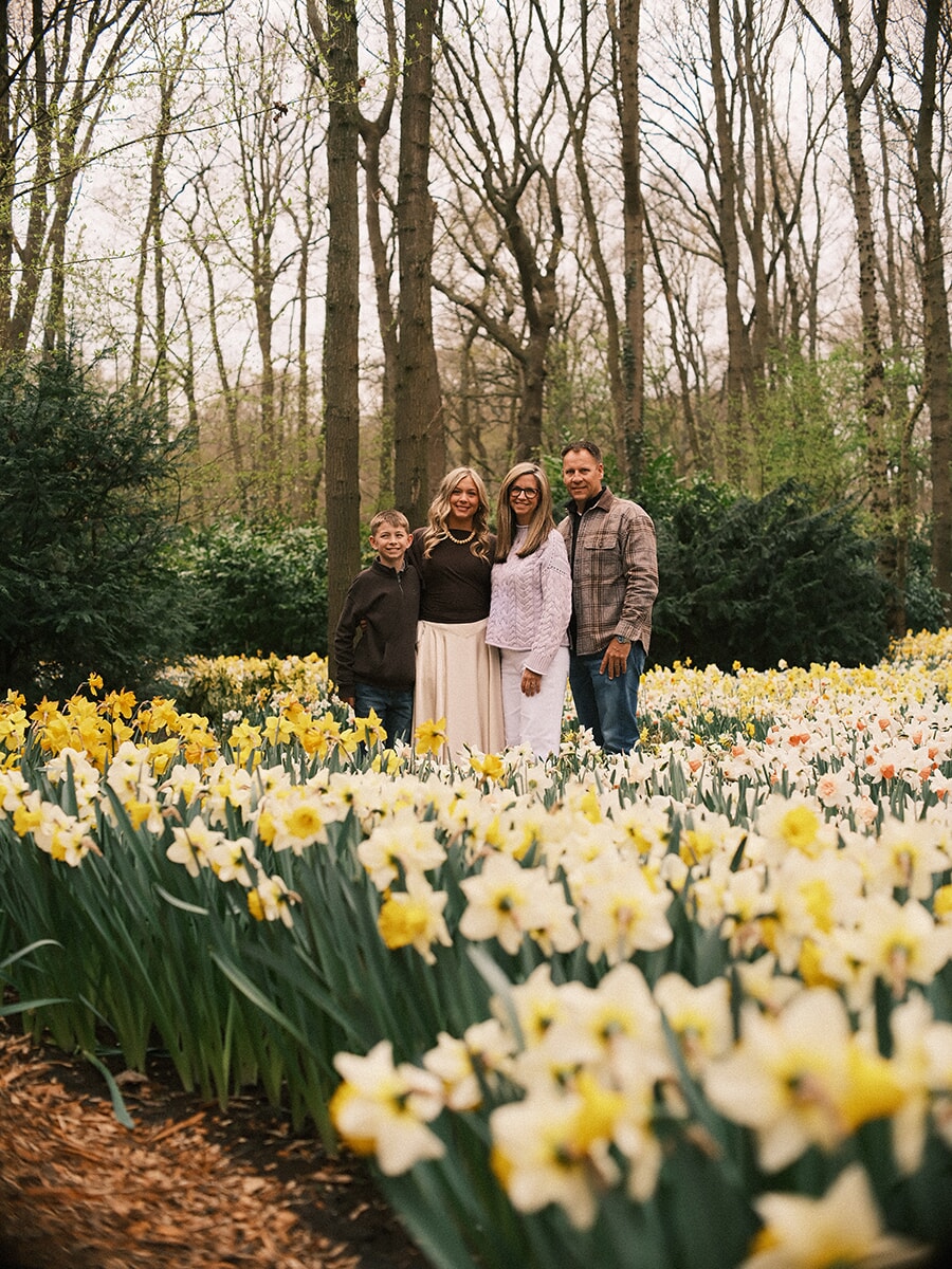 Family of four at the back of a vast drift of white and yellow daffodils, bare trees rising behind them