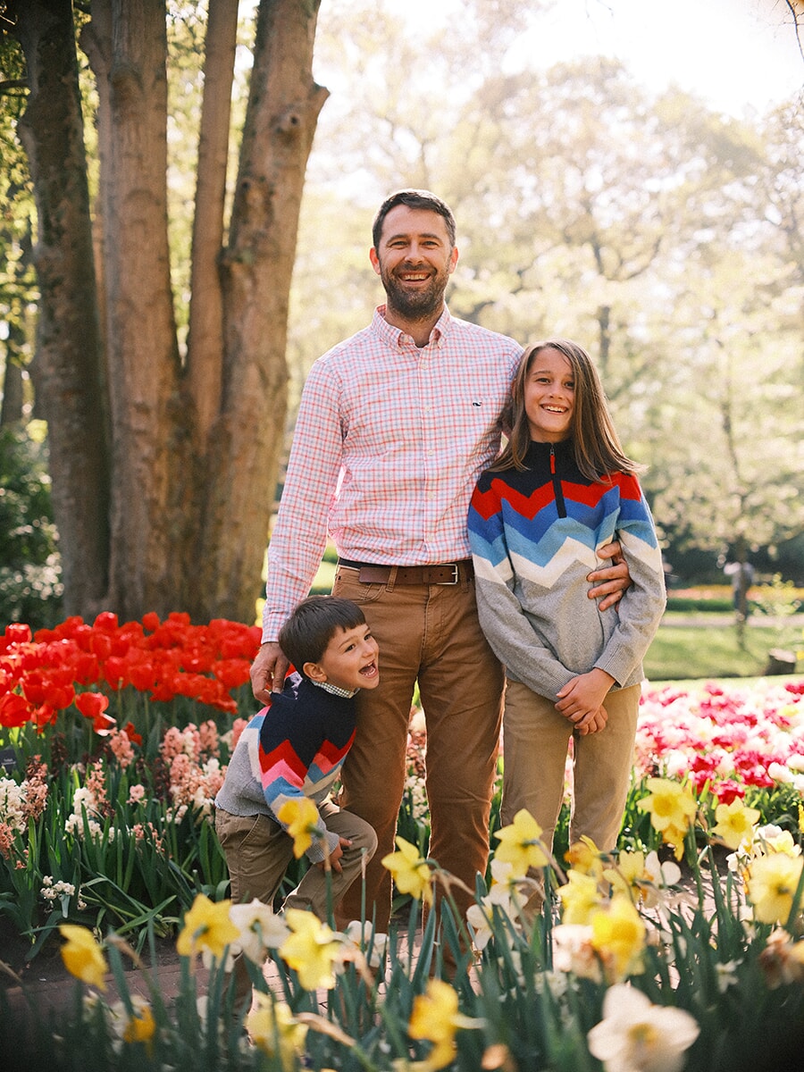 Father with his two children in front of a big tree, red tulips and daffodils around them during a family session at Keukenhof