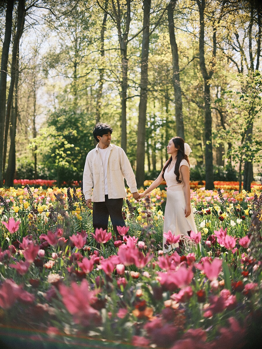 Holding hands and smiling at each other in a bed of pink tulips, a loveshoot at Keukenhof in soft spring light