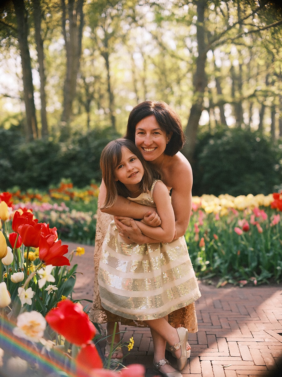 Mother hugging her young daughter from behind on a brick path, red and yellow tulips in front at Keukenhof