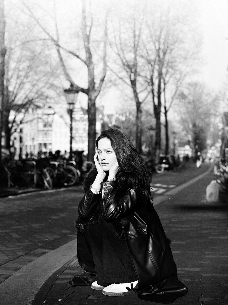 Analog street portrait in Amsterdam of a woman crouching on a brick pavement with her face resting in her hands