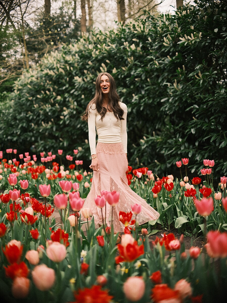 Woman in a flowing pink skirt laughing as she walks through pink and red tulips during her portrait photoshoot at Keukenhof