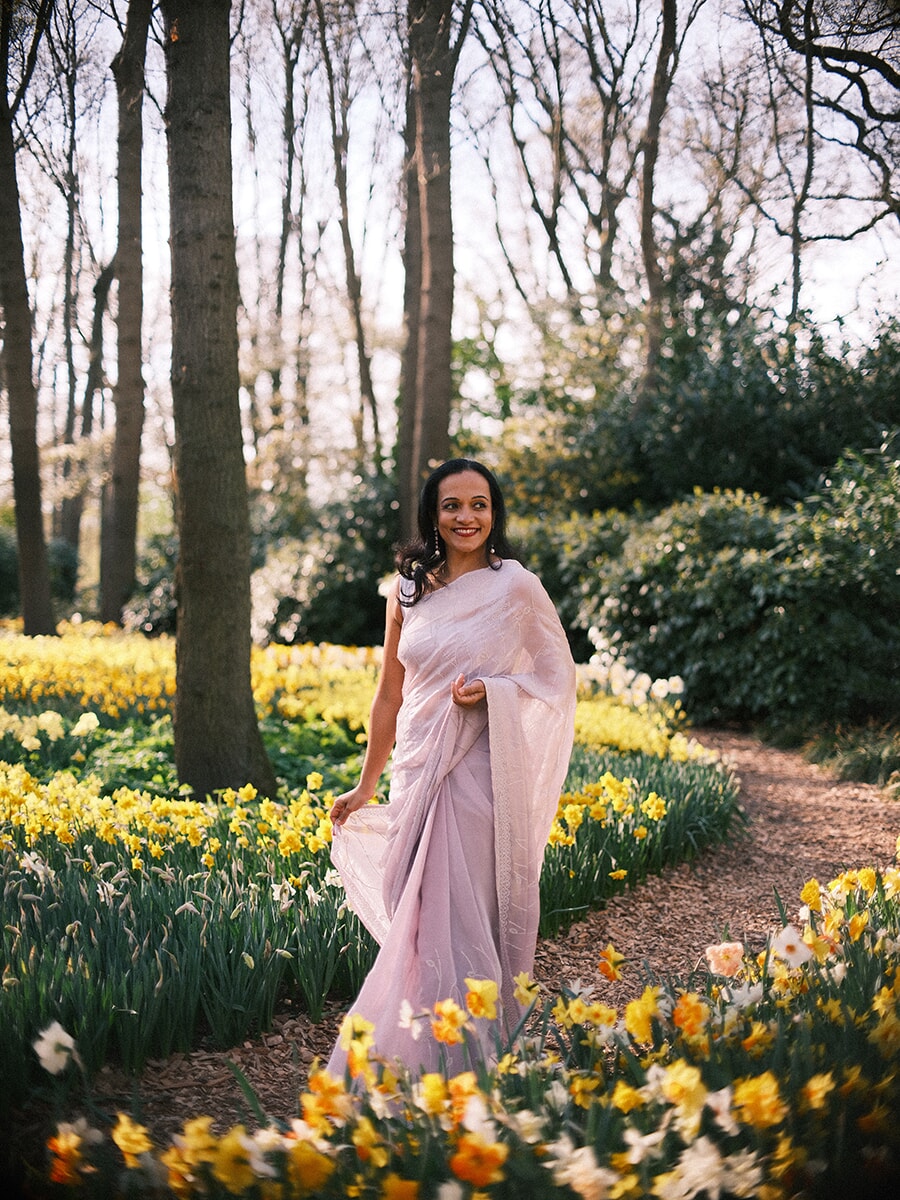 Woman in a pale pink draped dress walking a winding path between daffodils, a natural portrait photoshoot at Keukenhof